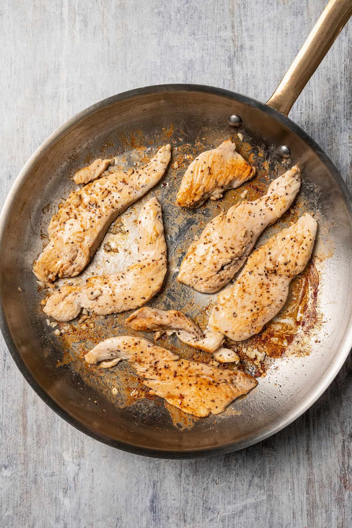 This chicken and bacon pasta is a 20-minute meal with tender linguine, juicy chicken, bacon, and parmesan in a creamy, Carbonara-style sauce. Chicken strips cooking in a skillet with bacon fat.