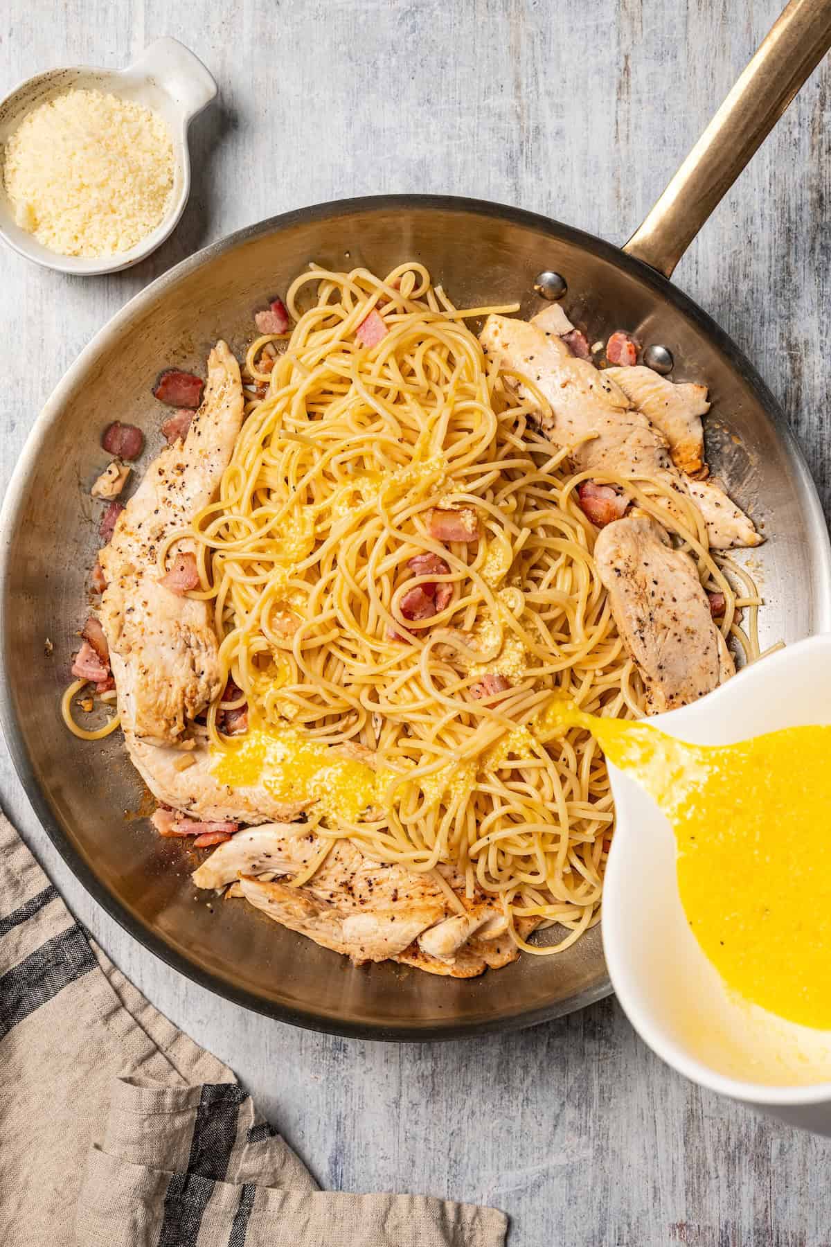 This chicken and bacon pasta is a 20-minute meal with tender linguine, juicy chicken, bacon, and parmesan in a creamy, Carbonara-style sauce. Pouring the egg sauce over chicken, bacon, and pasta in a skillet.