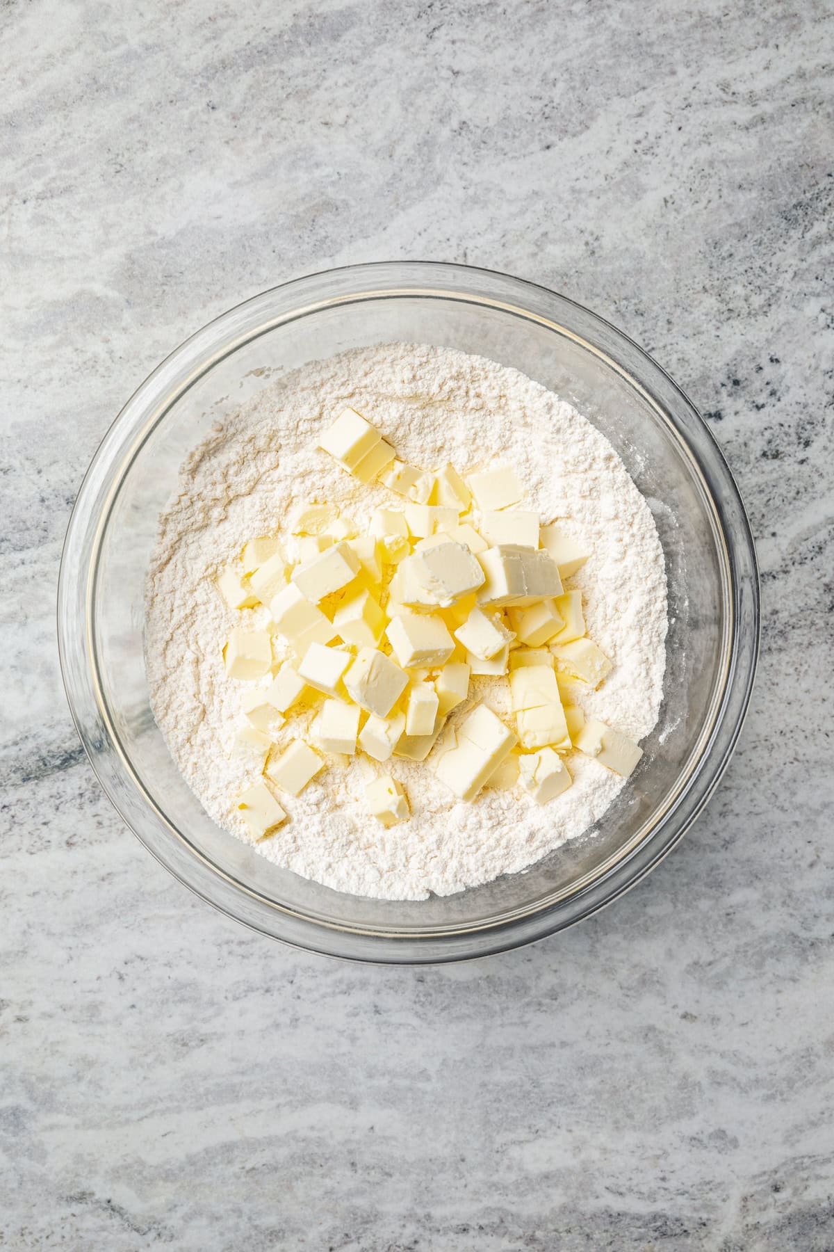 Cubed butter added to dry scone ingredients in a bowl.