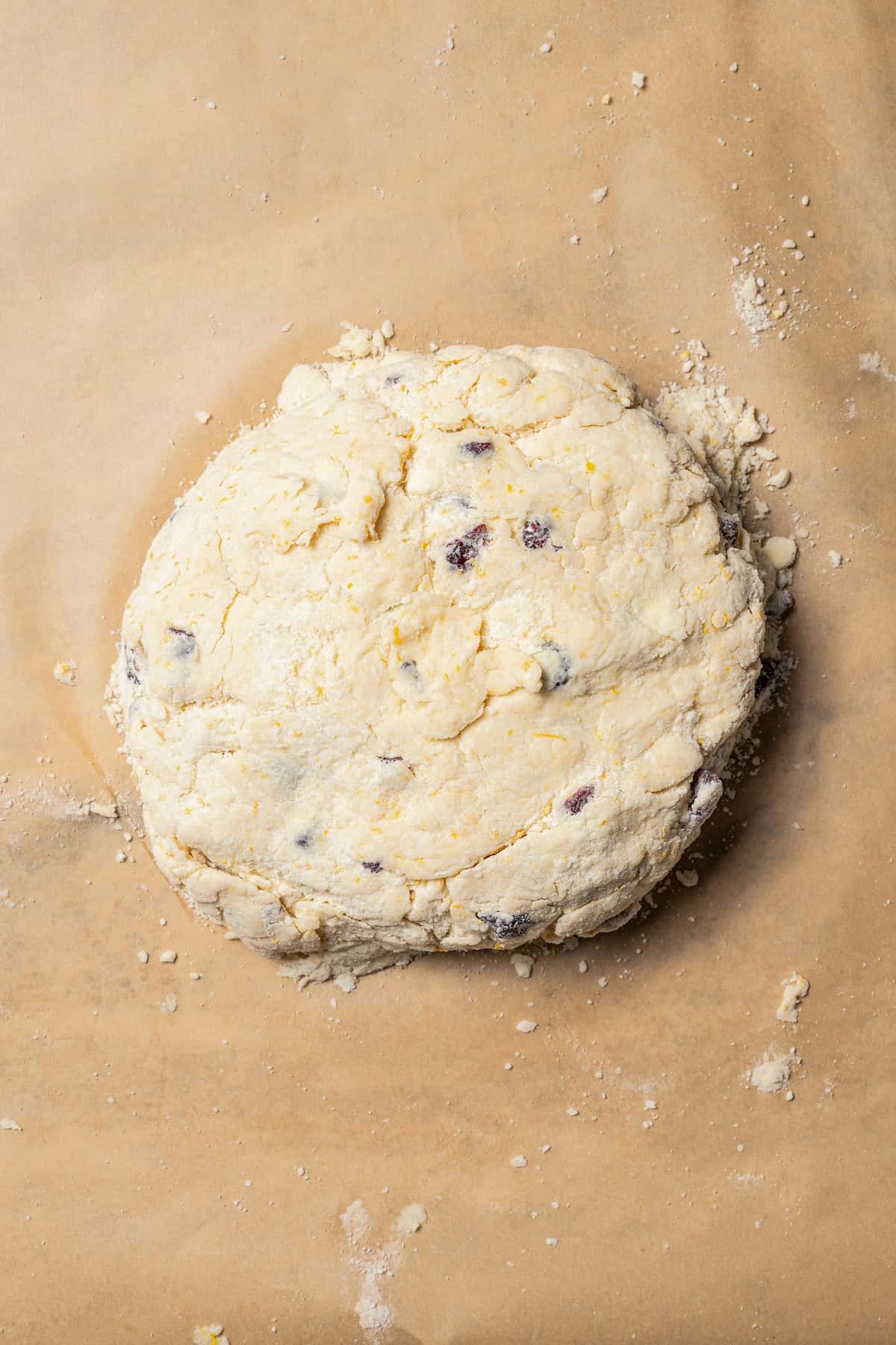 A large ball of cranberry orange scone dough on a sheet of parchment paper.