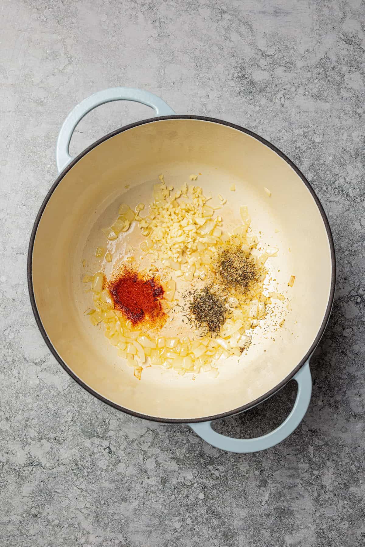 Braised potatoes are slow-cooked with tender green beans and tomatoes in this easy, one-pot Macedonian dish that warms from the inside out. Diced onion, garlic, and seasonings added to a pot.