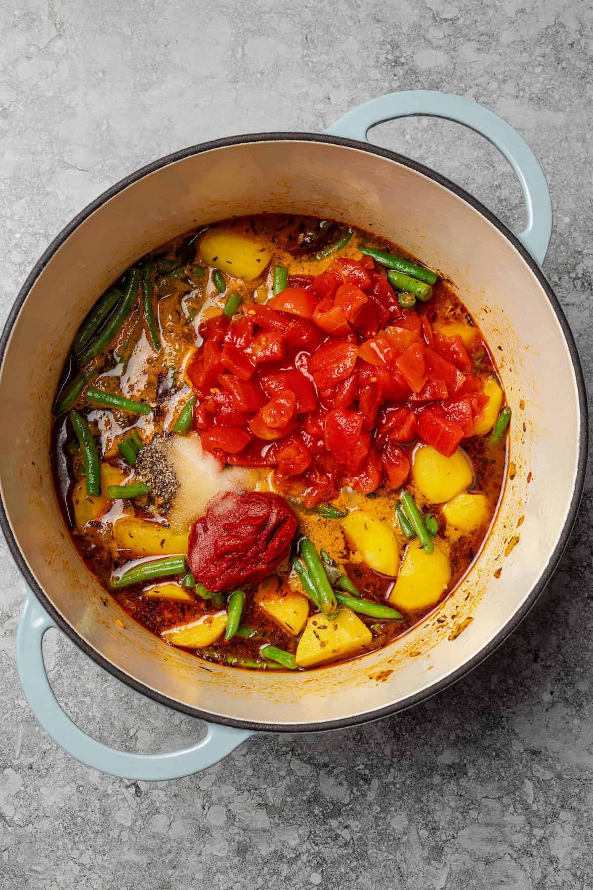 Braised potatoes are slow-cooked with tender green beans and tomatoes in this easy, one-pot Macedonian dish that warms from the inside out. Diced tomatoes, tomato paste, and seasonings added to a pot with potatoes and green beans.