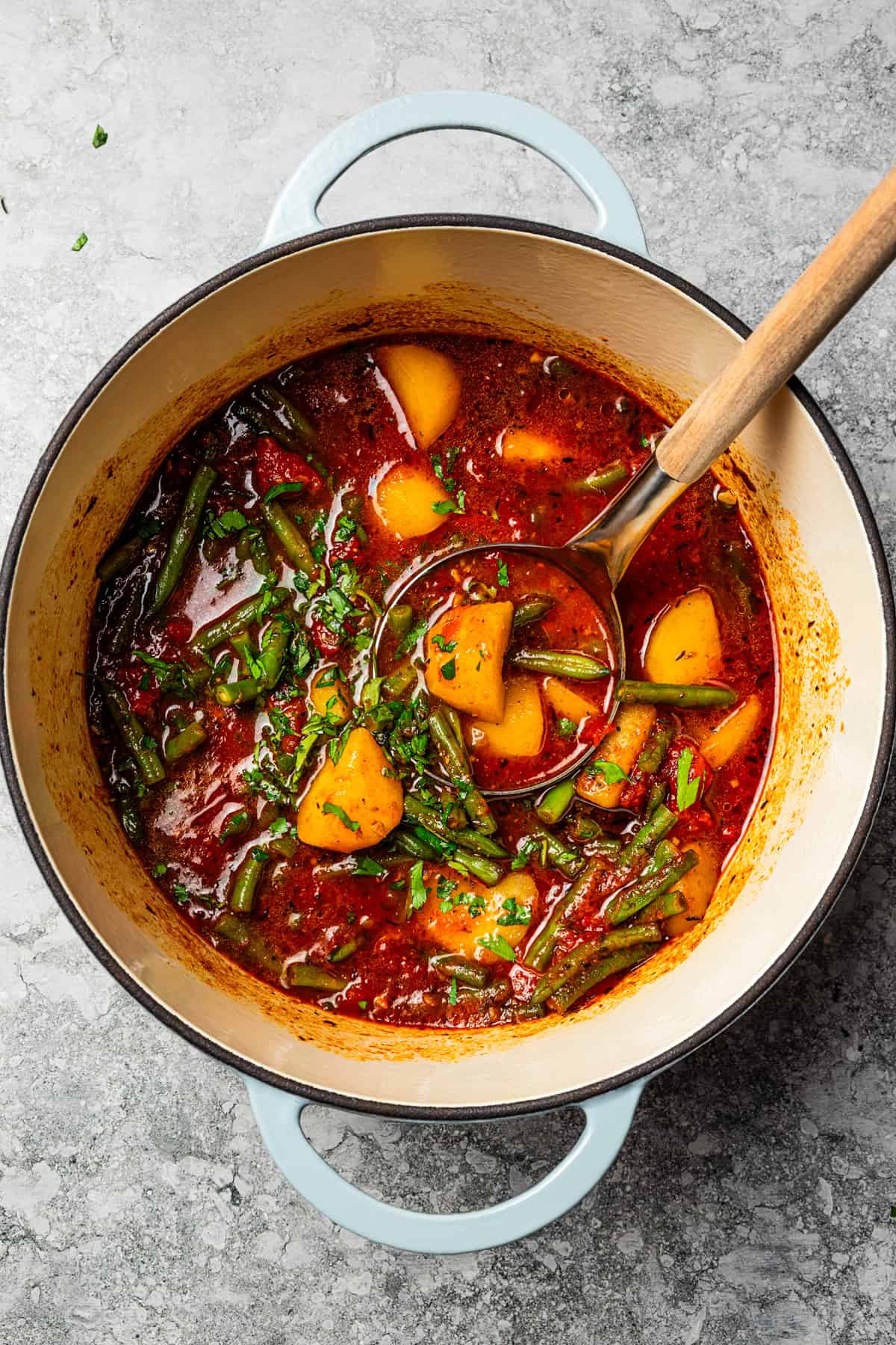 Braised potatoes are slow-cooked with tender green beans and tomatoes in this easy, one-pot Macedonian dish that warms from the inside out. Braised potatoes in a pot, with a ladle resting in the broth.