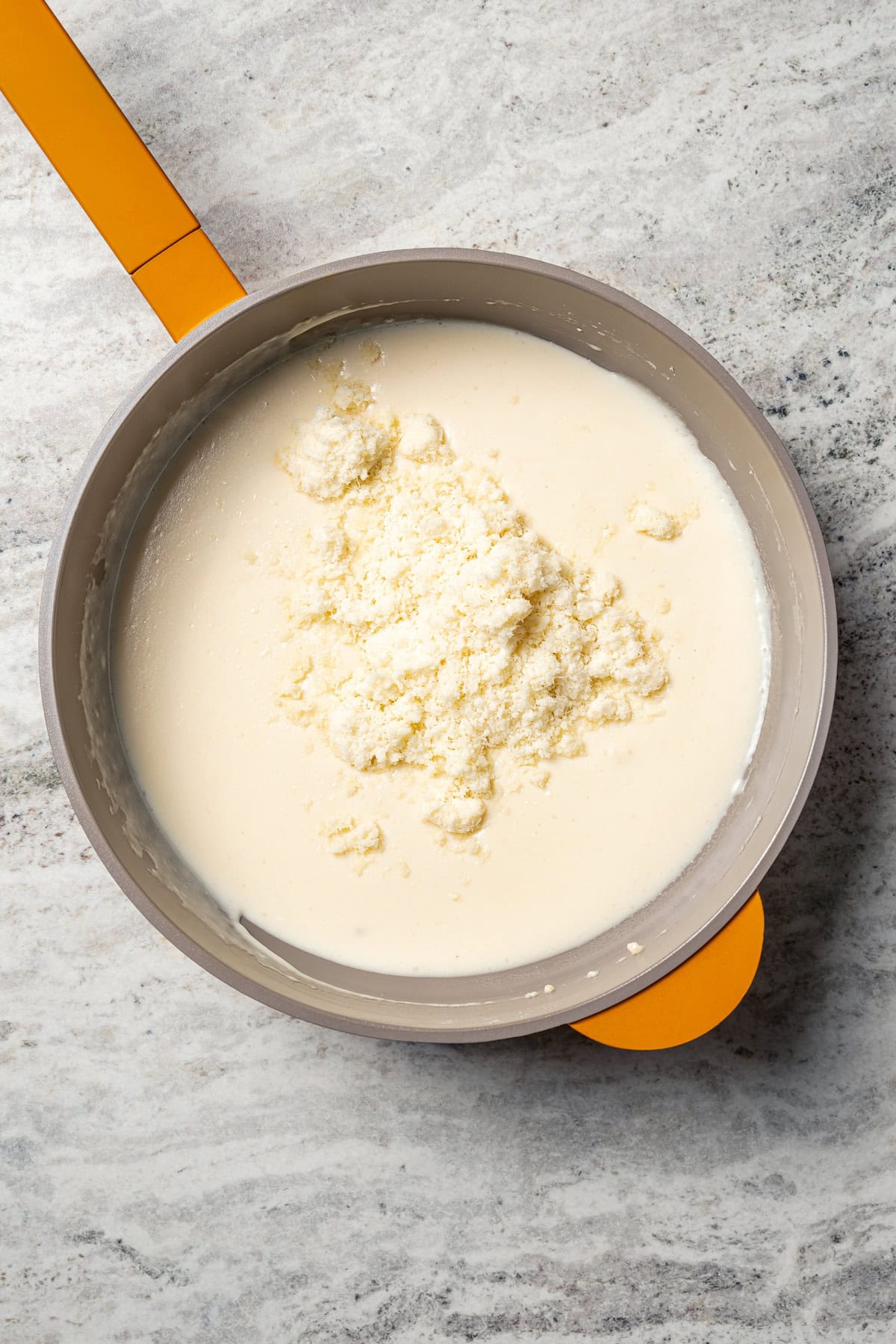 This easy scalloped potatoes recipe has thinly sliced potatoes smothered and baked in a flavorful cream sauce with nutmeg and Gruyère cheese. Grated Gruyere cheese added to cream sauce in a saucepan.