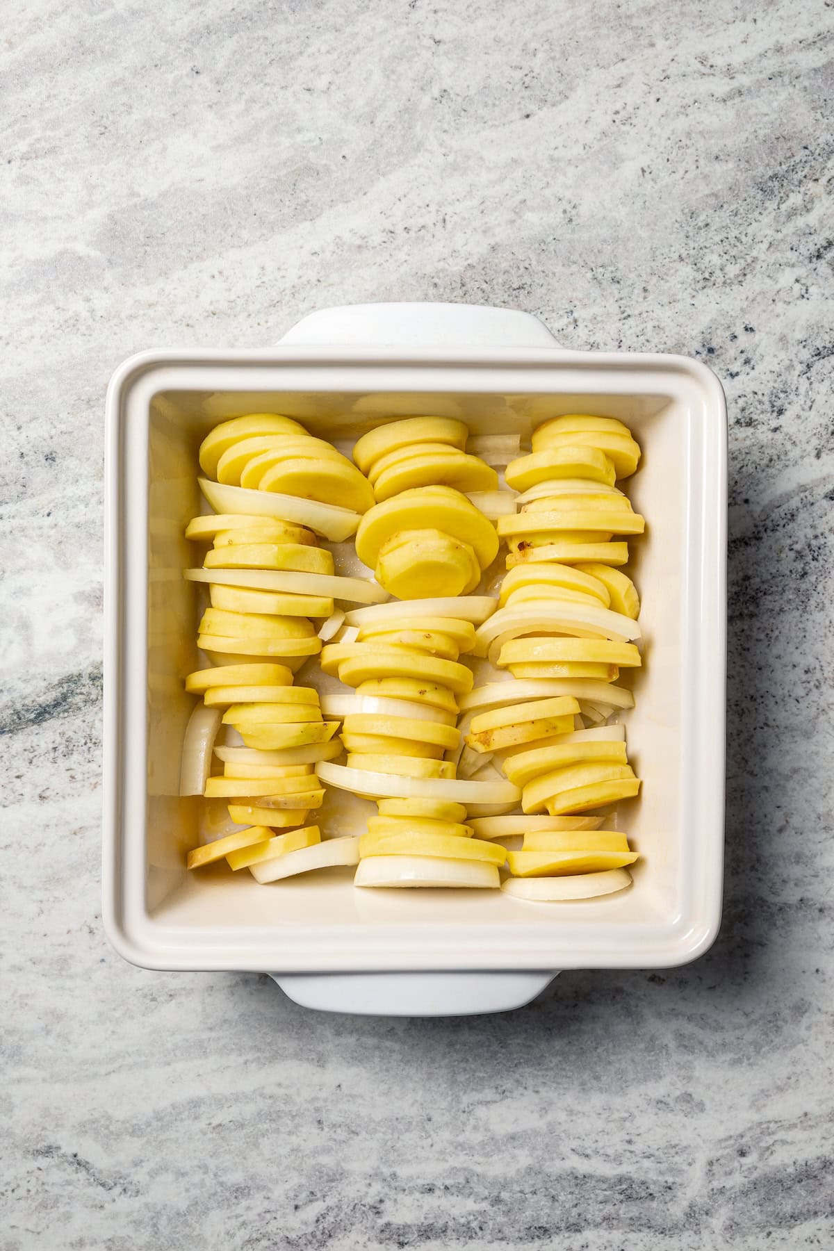 This easy scalloped potatoes recipe has thinly sliced potatoes smothered and baked in a flavorful cream sauce with nutmeg and Gruyère cheese. Potato slices arranged in rows inside a baking dish.