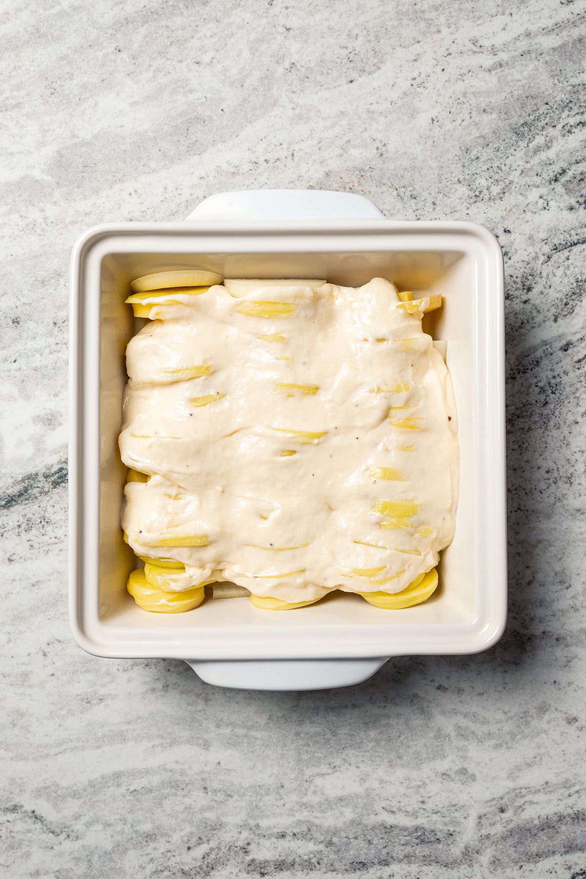 This easy scalloped potatoes recipe has thinly sliced potatoes smothered and baked in a flavorful cream sauce with nutmeg and Gruyère cheese. Cheese sauce layered over sliced potatoes in a baking dish.