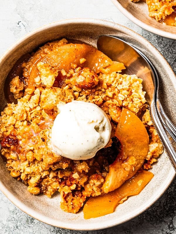 A bowl of apple crisp topped with scoops of vanilla ice cream.