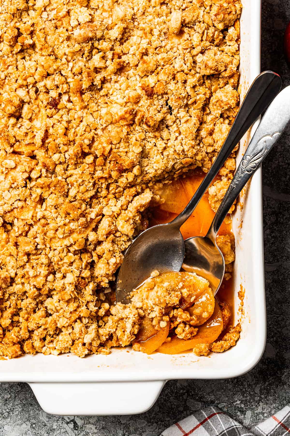 This old-fashioned apple crisp is a classic dessert, with apples, real apple cider, and warm spices baked under a light, crispy oat topping. Spooning out apple crisp from a baking dish.