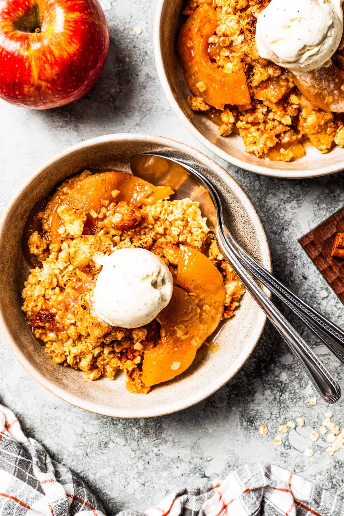 This old-fashioned apple crisp is a classic dessert, with apples, real apple cider, and warm spices baked under a light, crispy oat topping. Two bowls of apple crisp topped with ice cream.