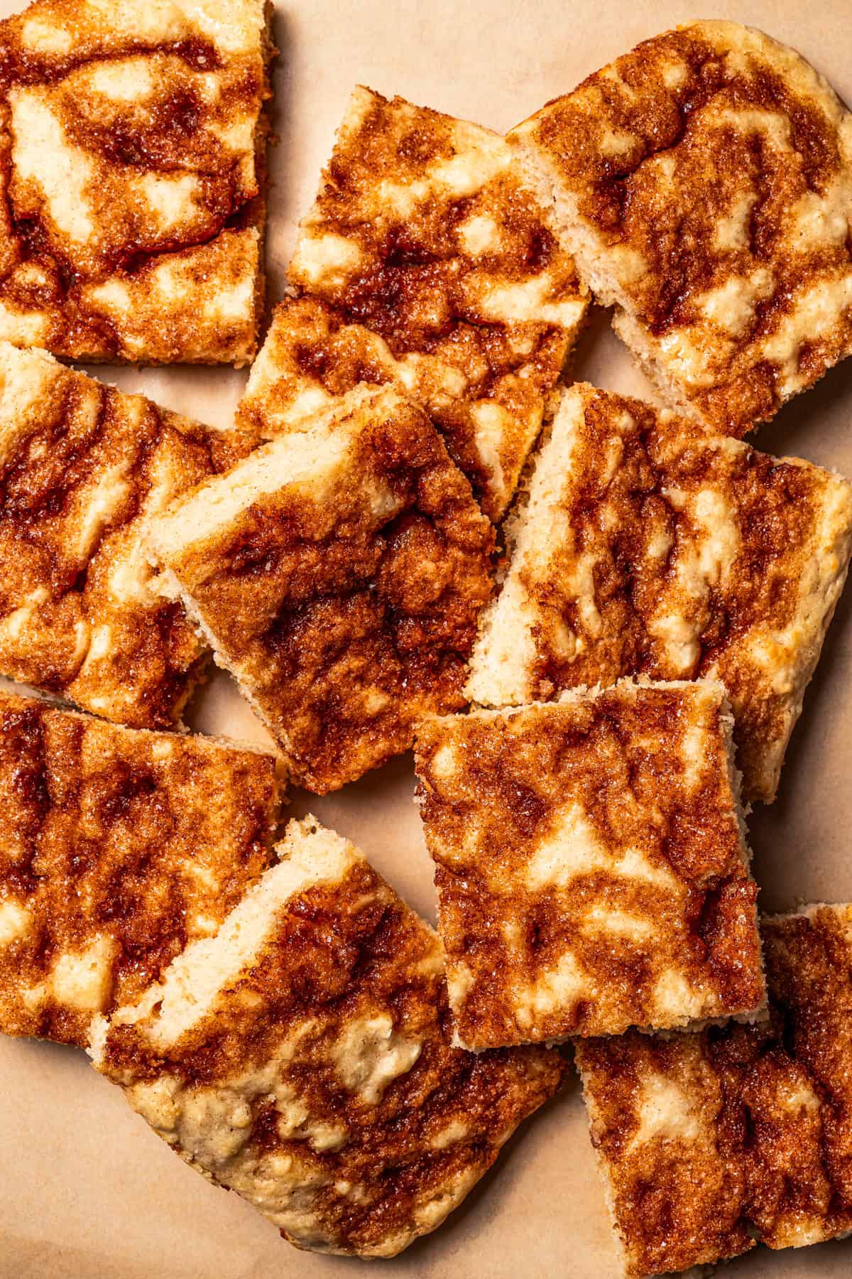 Cinnamon roll sheet pan pancakes cut into squares, scattered on a sheet of brown parchment paper.