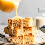 Pouring glaze over a stack of fluffy cinnamon roll sheet pan pancakes on a plate.
