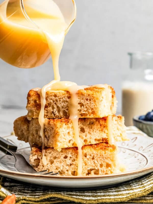 Pouring glaze over a stack of fluffy cinnamon roll sheet pan pancakes on a plate.