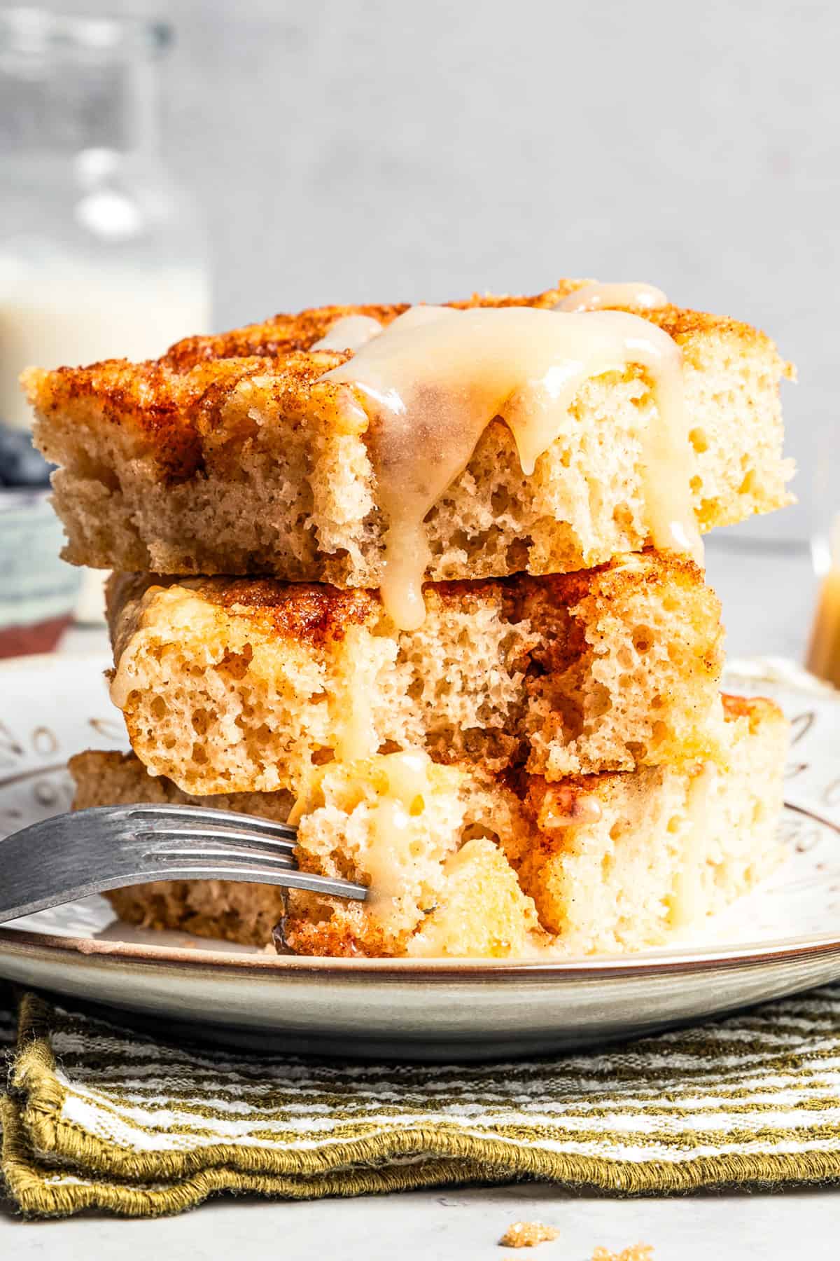 Three thick cinnamon roll sheet pan pancakes stacked on a plate, with a forkful resting on the side.