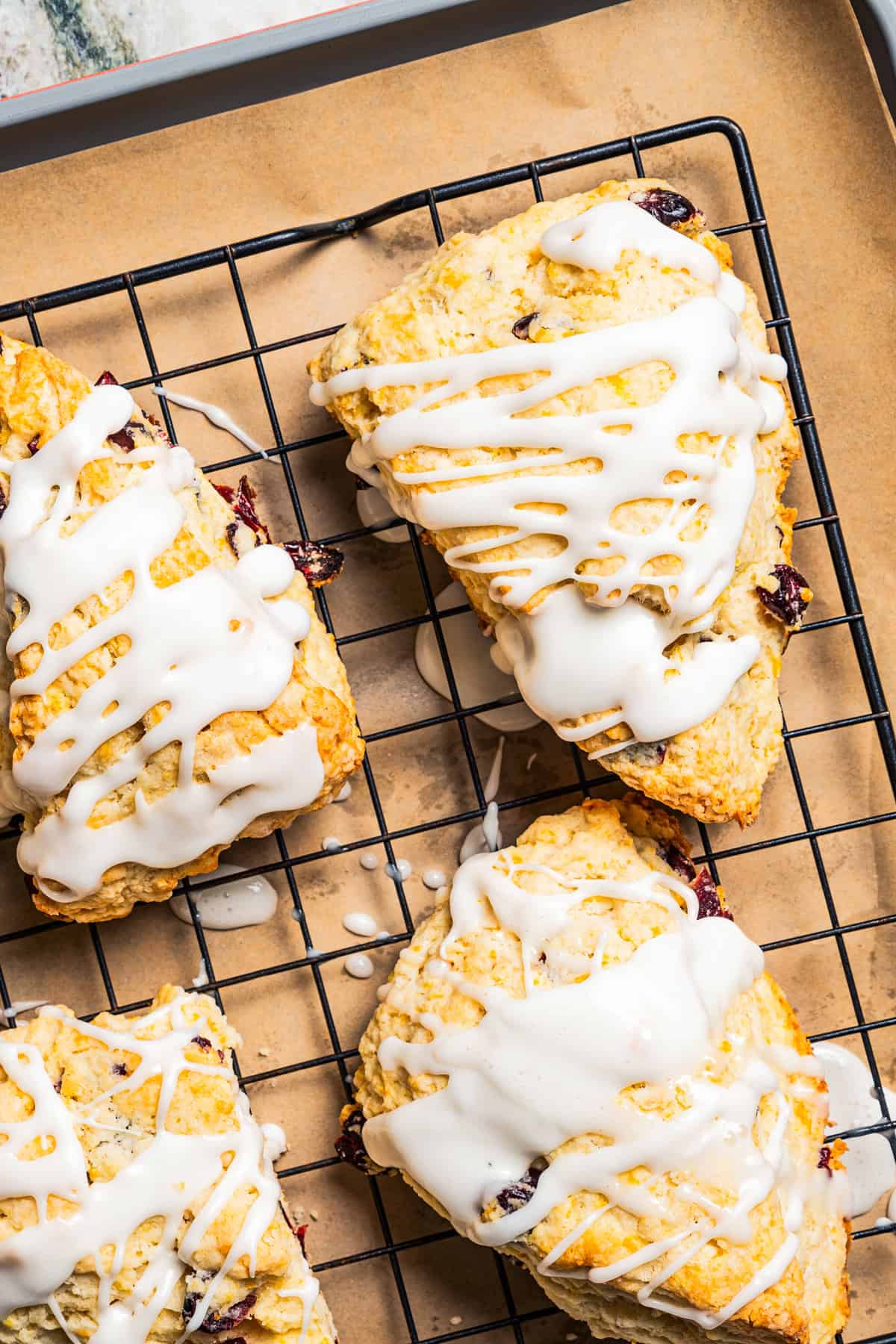 Glazed cranberry orange scones are cooling on a wire rack.