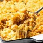 A spoon lifting a serving of gooey, melty baked mac and cheese from a casserole dish of homemade mac and cheese.