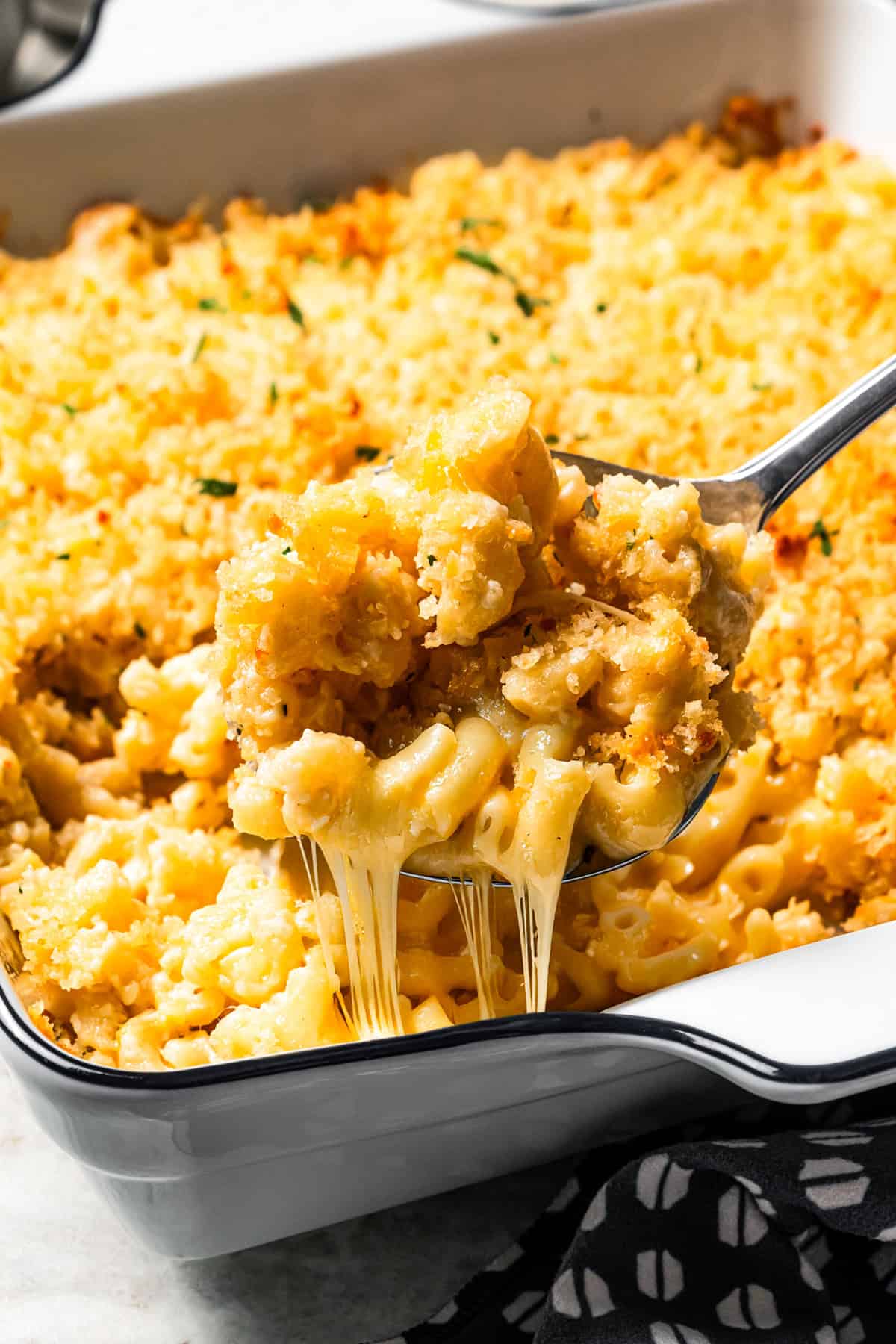 This easy baked mac and cheese recipe has tender pasta and a creamy, melty homemade cheese sauce, baked until golden and bubbly in the oven! A spoon lifting a serving of gooey, melty baked mac and cheese from a casserole dish of homemade mac and cheese.