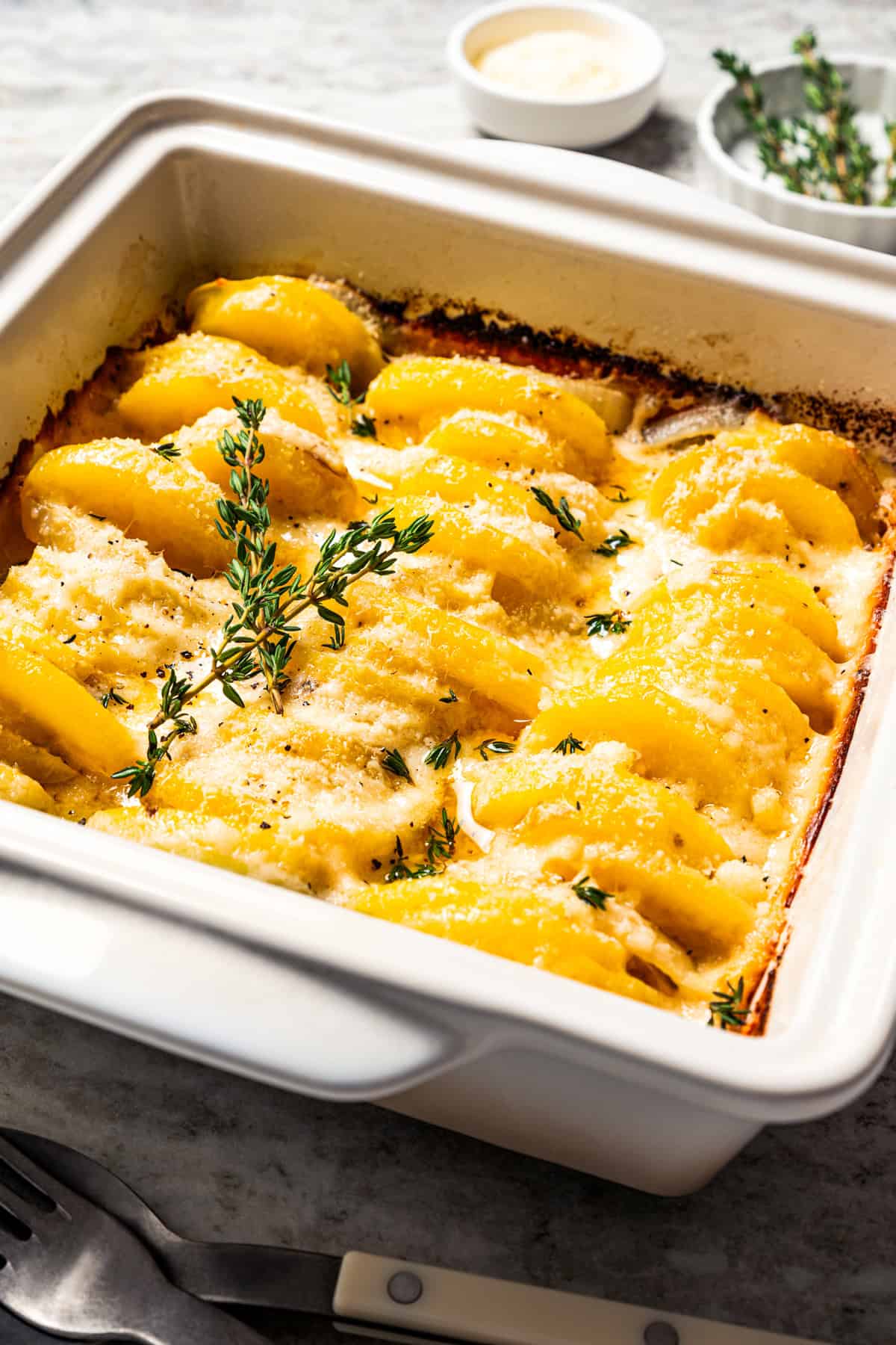 This easy scalloped potatoes recipe has thinly sliced potatoes smothered and baked in a flavorful cream sauce with nutmeg and Gruyère cheese. Scalloped potatoes in a white casserole dish.