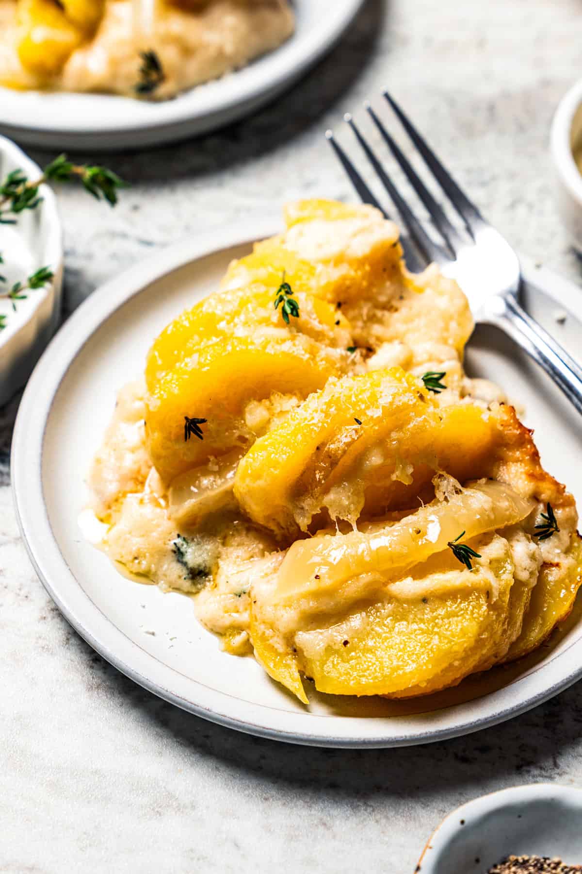 This easy scalloped potatoes recipe has thinly sliced potatoes smothered and baked in a flavorful cream sauce with nutmeg and Gruyère cheese. Scalloped potatoes served on a dish.