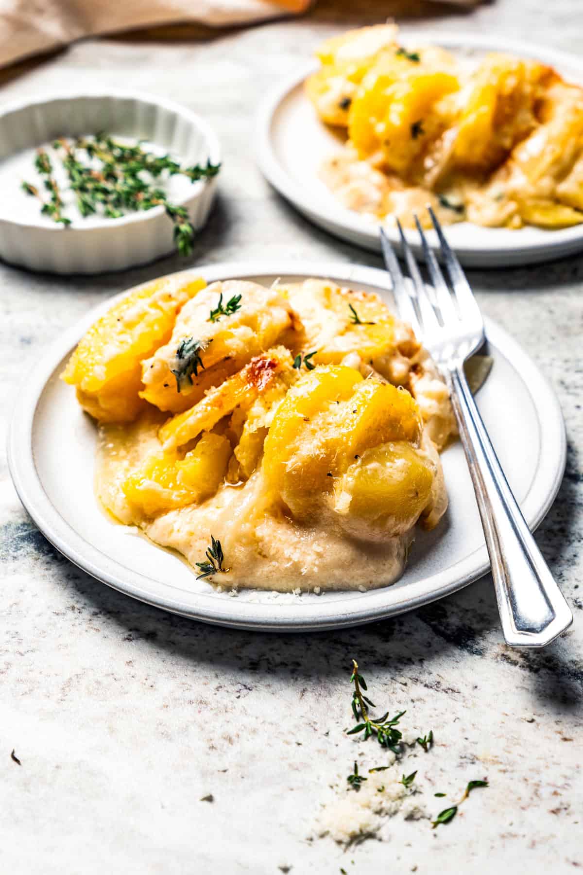 This easy scalloped potatoes recipe has thinly sliced potatoes smothered and baked in a flavorful cream sauce with nutmeg and Gruyère cheese. Scalloped potatoes served on a dish with a fork placed next to the potatoes.