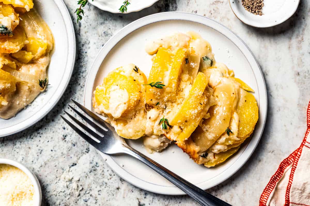 This easy scalloped potatoes recipe has thinly sliced potatoes smothered and baked in a flavorful cream sauce with nutmeg and Gruyère cheese. Scalloped potatoes served on a dinner plate.