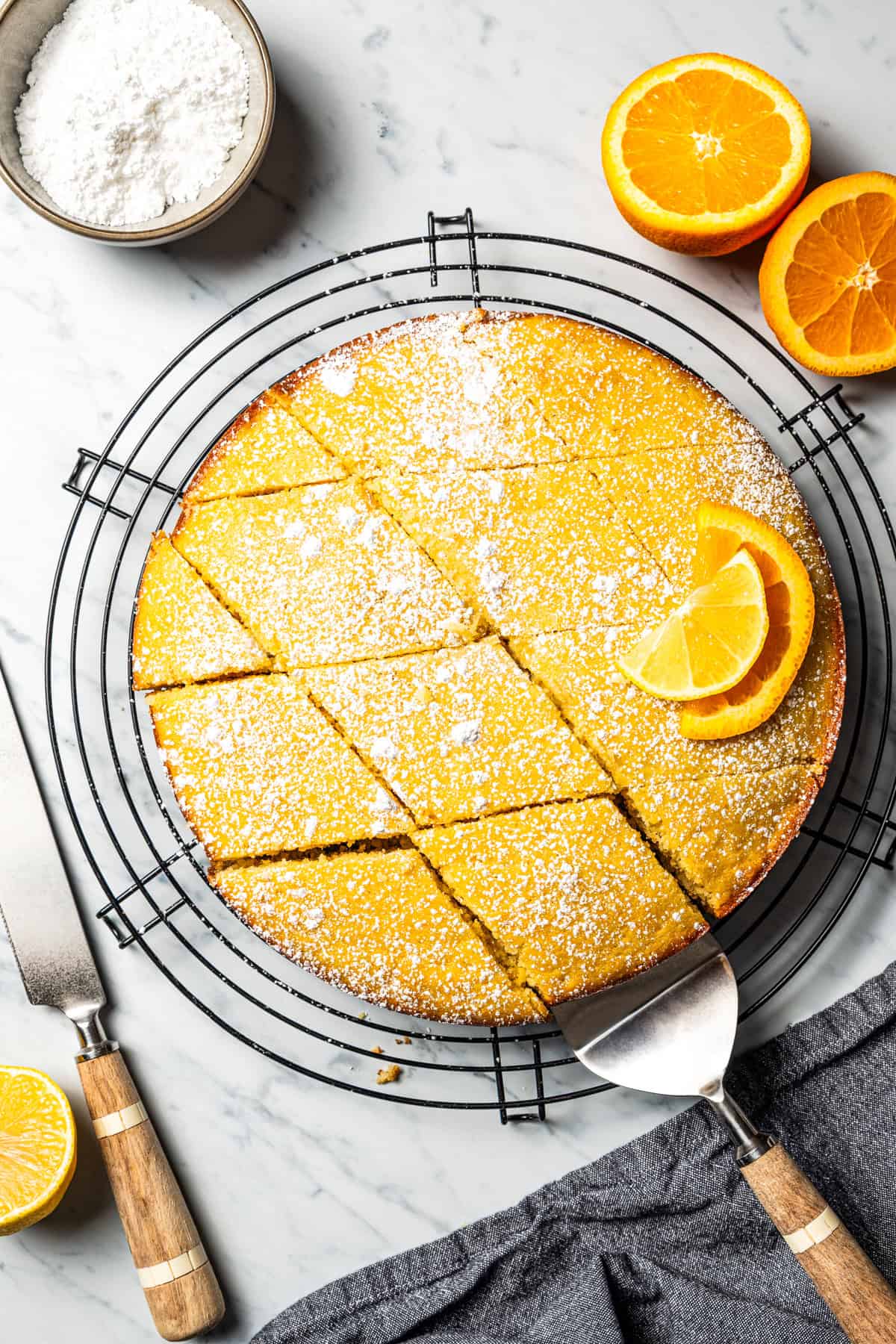 Macedonian semolina cake cut into diamond-shaped slices, topped with powdered sugar and two orange slices.