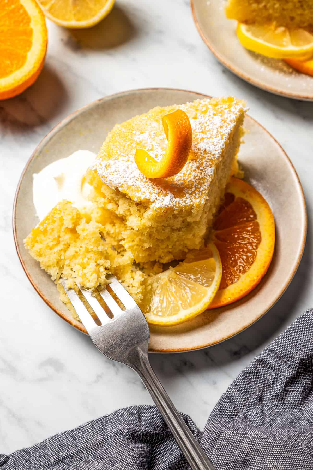 A forkful of semolina cake next to a slice of cake topped with an orange rind.