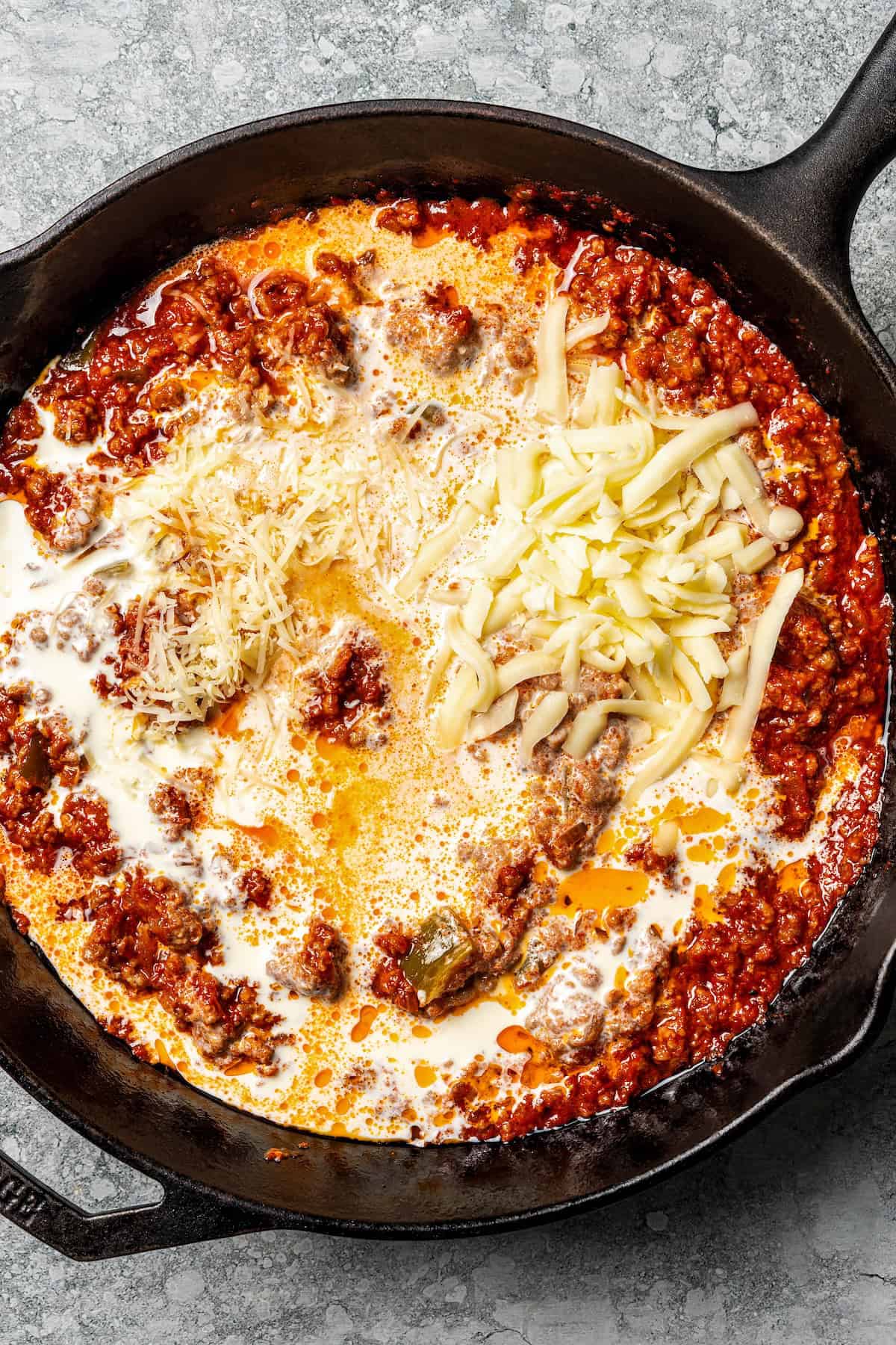 My easy baked ziti recipe is a weeknight-friendly pasta casserole with rich homemade meat sauce and three kinds of melty Italian cheese. Shredded cheese added to meat sauce in a skillet.