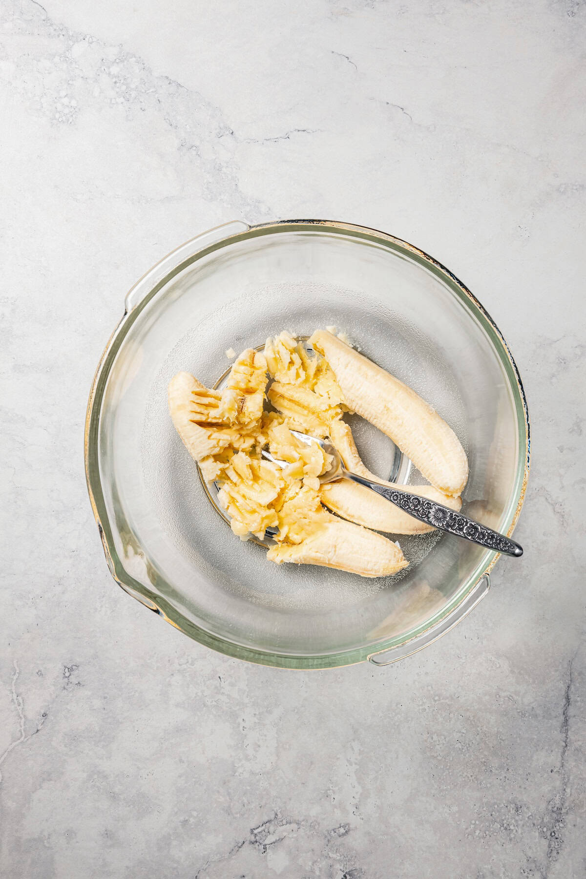 Partially mashed bananas in a glass bowl with a fork.