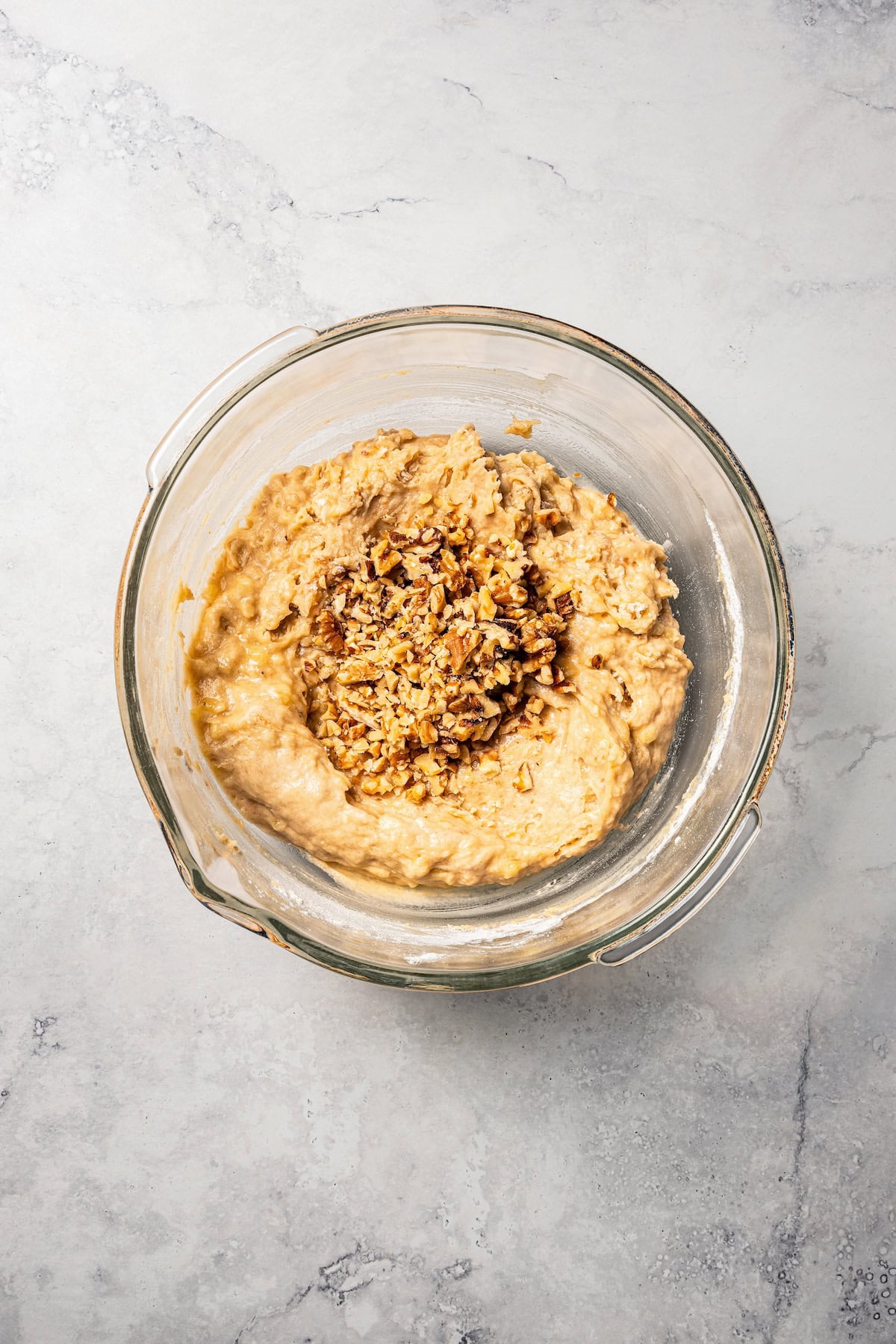Chopped walnuts added to a bowl of banana muffin batter.