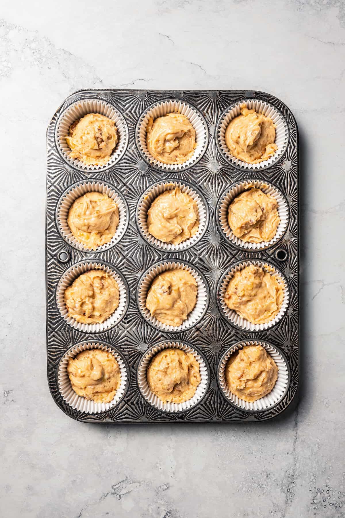Overhead view of a lined muffin pan filled with banana nut muffin batter.