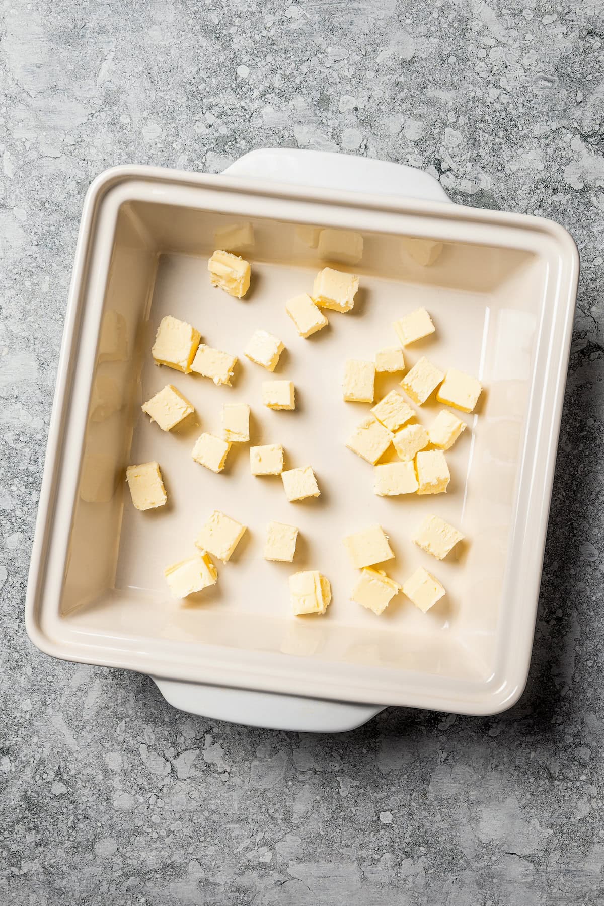Butter swim biscuits are fluffy drop biscuits baked in a pool of butter! Crispy outside, soft inside, and easy to make with 5 ingredients. Cubed butter scattered in the bottom of a baking dish.