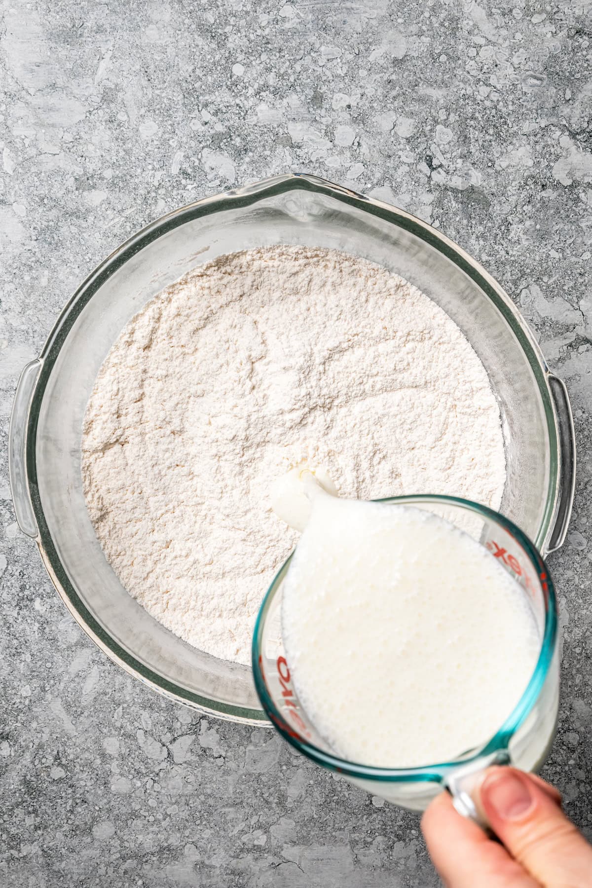 Butter swim biscuits are fluffy drop biscuits baked in a pool of butter! Crispy outside, soft inside, and easy to make with 5 ingredients. Wet ingredients being poured into a bowl of flour.