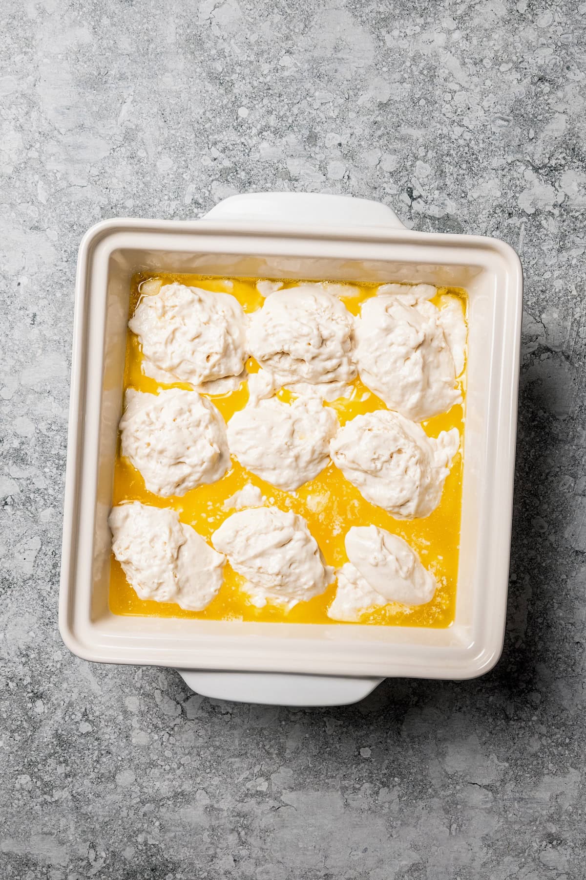 Butter swim biscuits are fluffy drop biscuits baked in a pool of butter! Crispy outside, soft inside, and easy to make with 5 ingredients. Scoops of biscuit batter added to melted butter in a square baking dish.