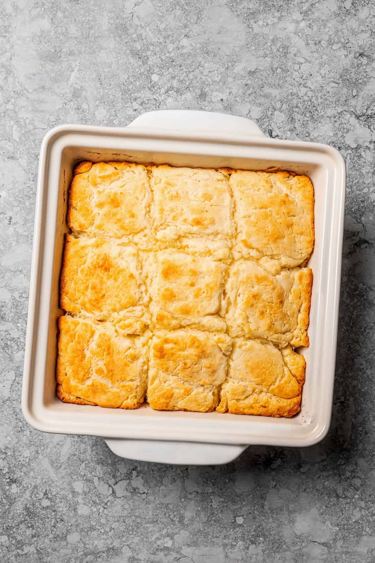 Butter swim biscuits are fluffy drop biscuits baked in a pool of butter! Crispy outside, soft inside, and easy to make with 5 ingredients. Overhead view of golden-baked butter swim biscuits in a square baking dish.