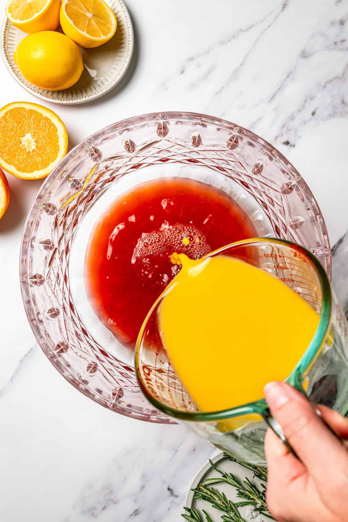 This festive Christmas punch recipe is the best big-batch cocktail to get your holiday party started this year. Make it boozy, or not! Orange juice being poured into a punch bowl with the rest of the juices.