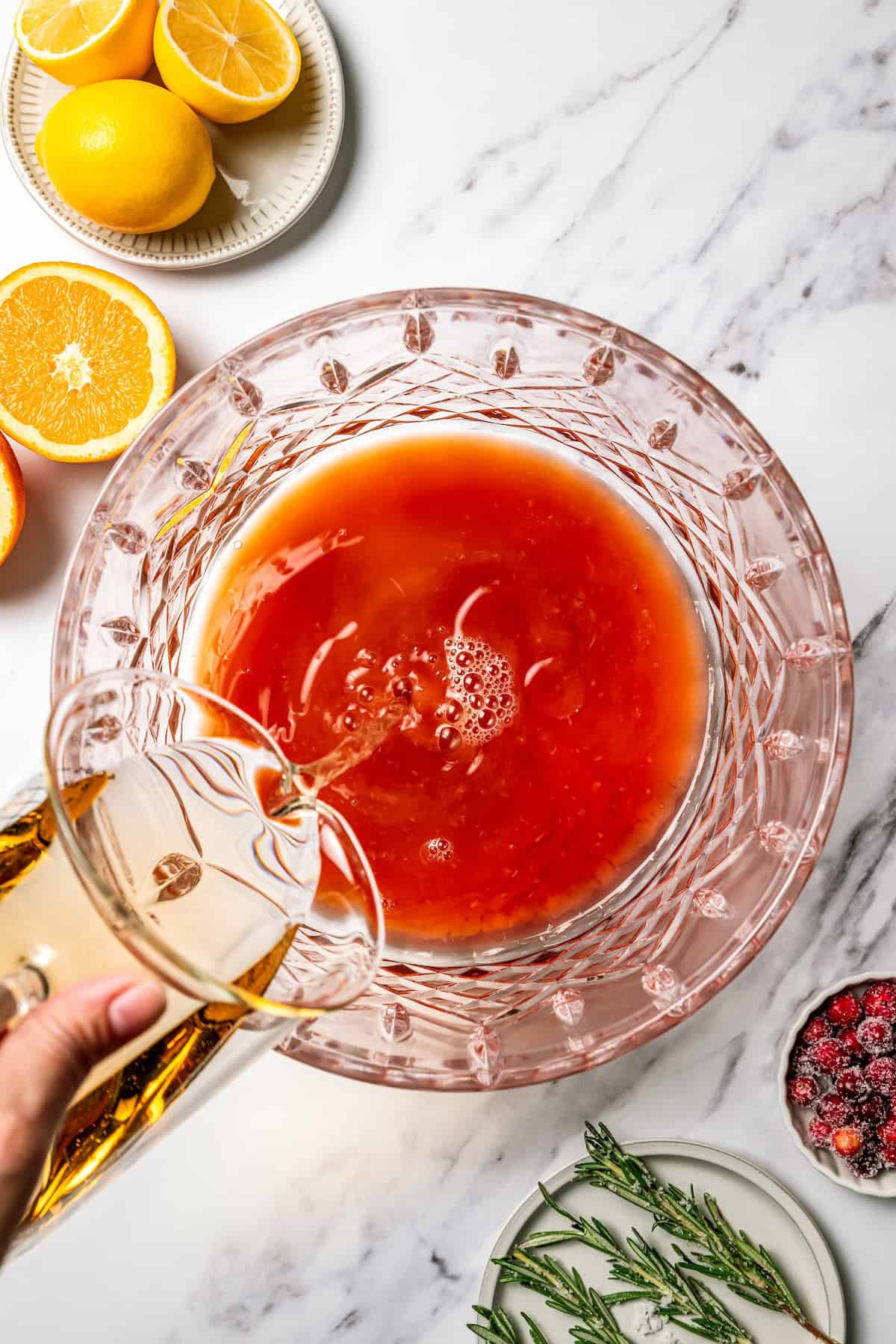 This festive Christmas punch recipe is the best big-batch cocktail to get your holiday party started this year. Make it boozy, or not! Ginger ale being poured into a punch bowl with the rest of the Christmas punch ingredients.