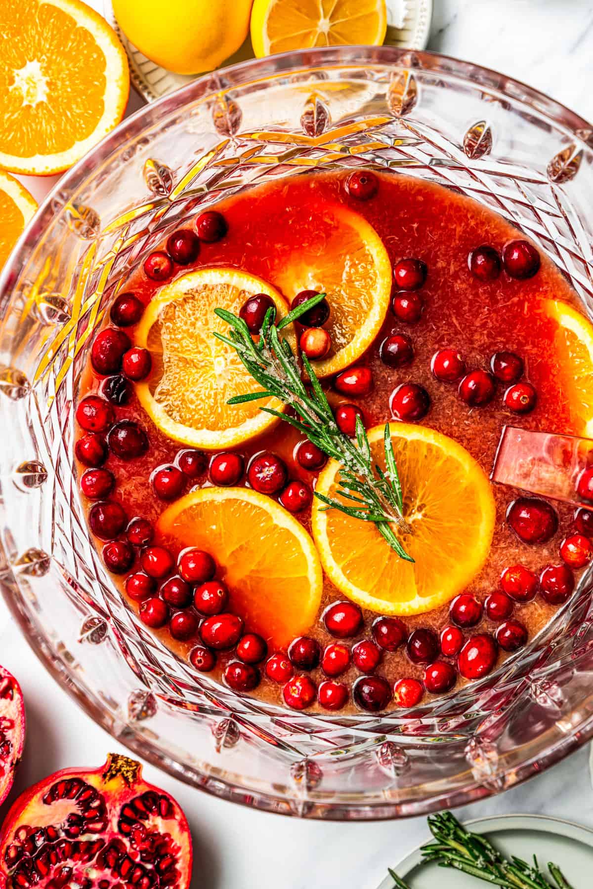 Christmas punch in a bowl, and it's garnished with orange slices, cranberries, and a rosemary sprig.