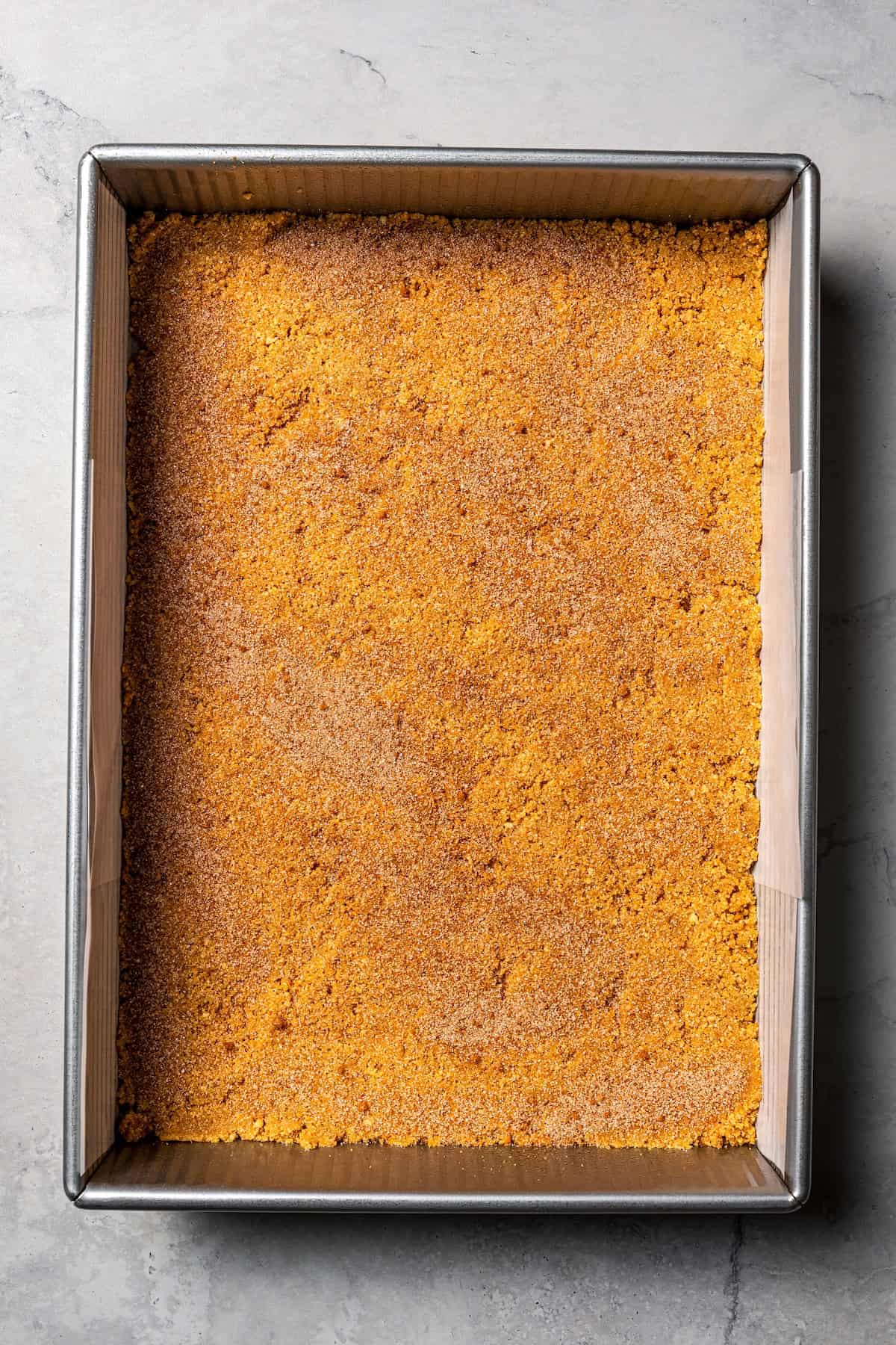 This churro cheesecake bars recipe is an easy dessert with layers of cinnamon sugar, a flaky pastry crust, and creamy cheesecake filling. Cinnamon sugar and cookie crumb crust pressed into the bottom of a baking pan.