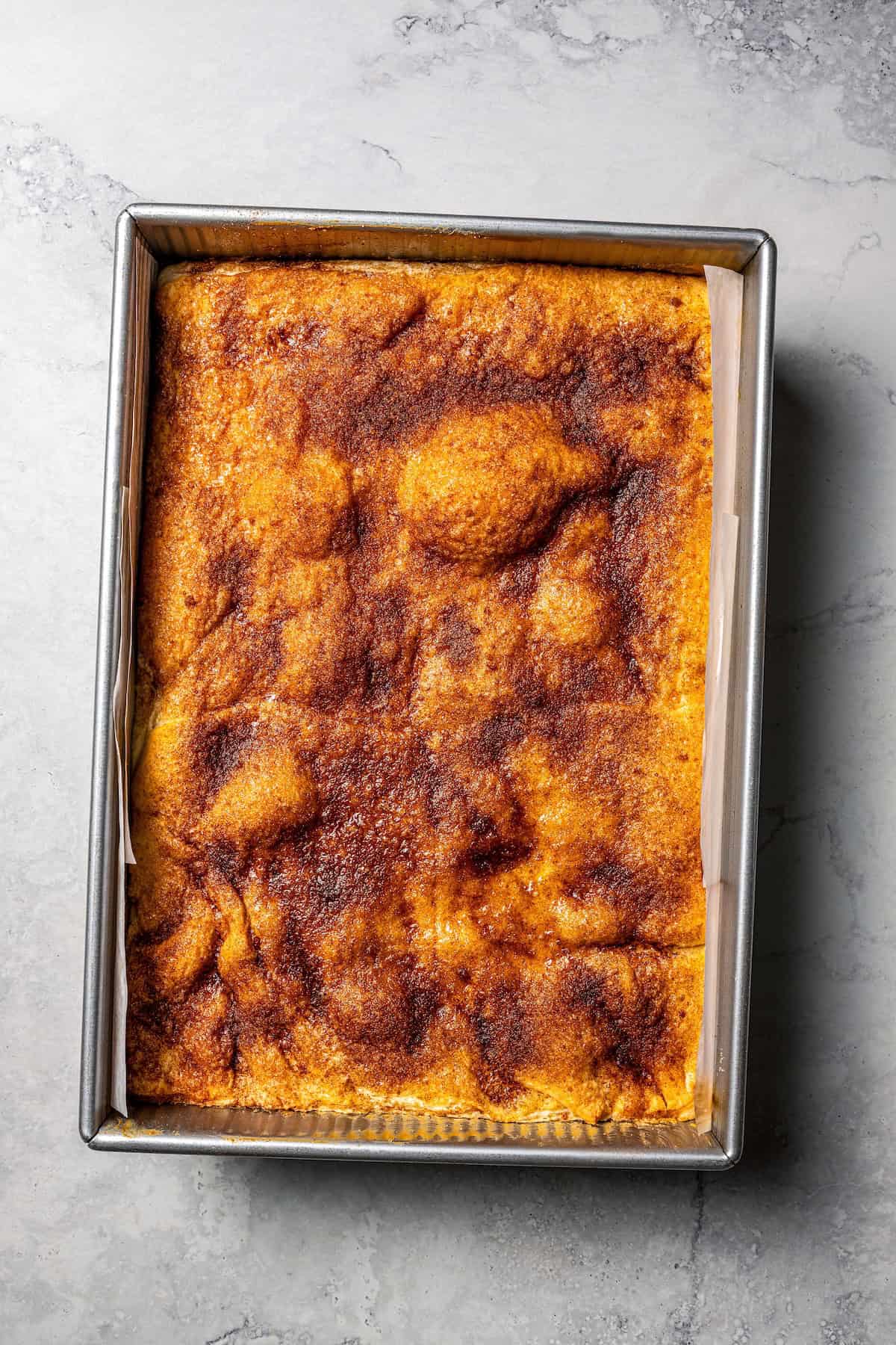 This churro cheesecake bars recipe is an easy dessert with layers of cinnamon sugar, a flaky pastry crust, and creamy cheesecake filling. Overhead view of churro cheesecake bars in a baking pan.