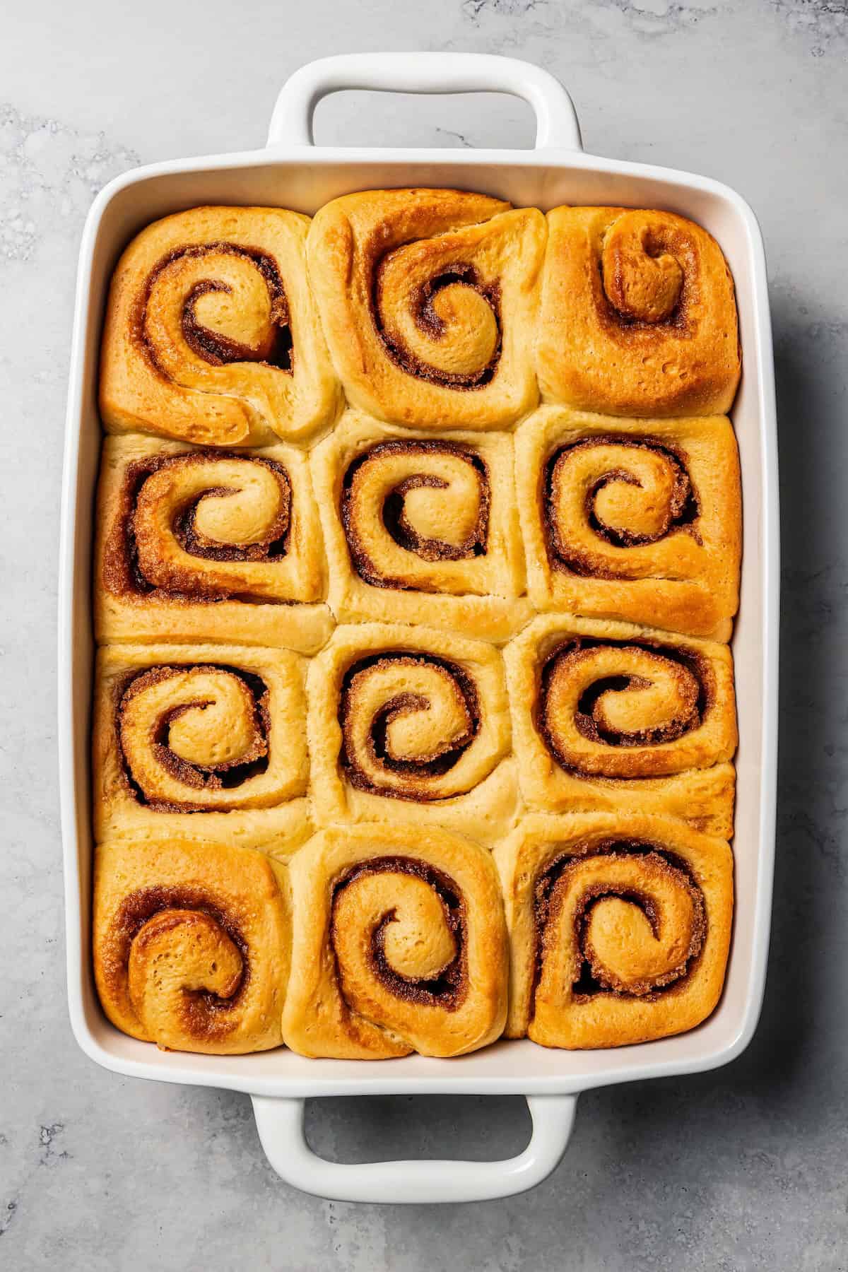 This cinnamon roll recipe makes big, bakery-style cinnamon buns filled with gooey cinnamon sugar and topped with sweet cream cheese frosting. Freshly baked cinnamon rolls in a baking dish.