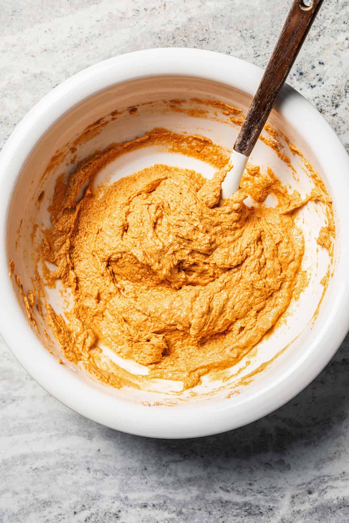 Pumpkin pancakes are the best fall breakfast! Made from pancake mix, real pumpkin, and spices, topped with cranberry syrup for the holidays. Pumpkin pancake batter in a bowl with a wooden spoon.
