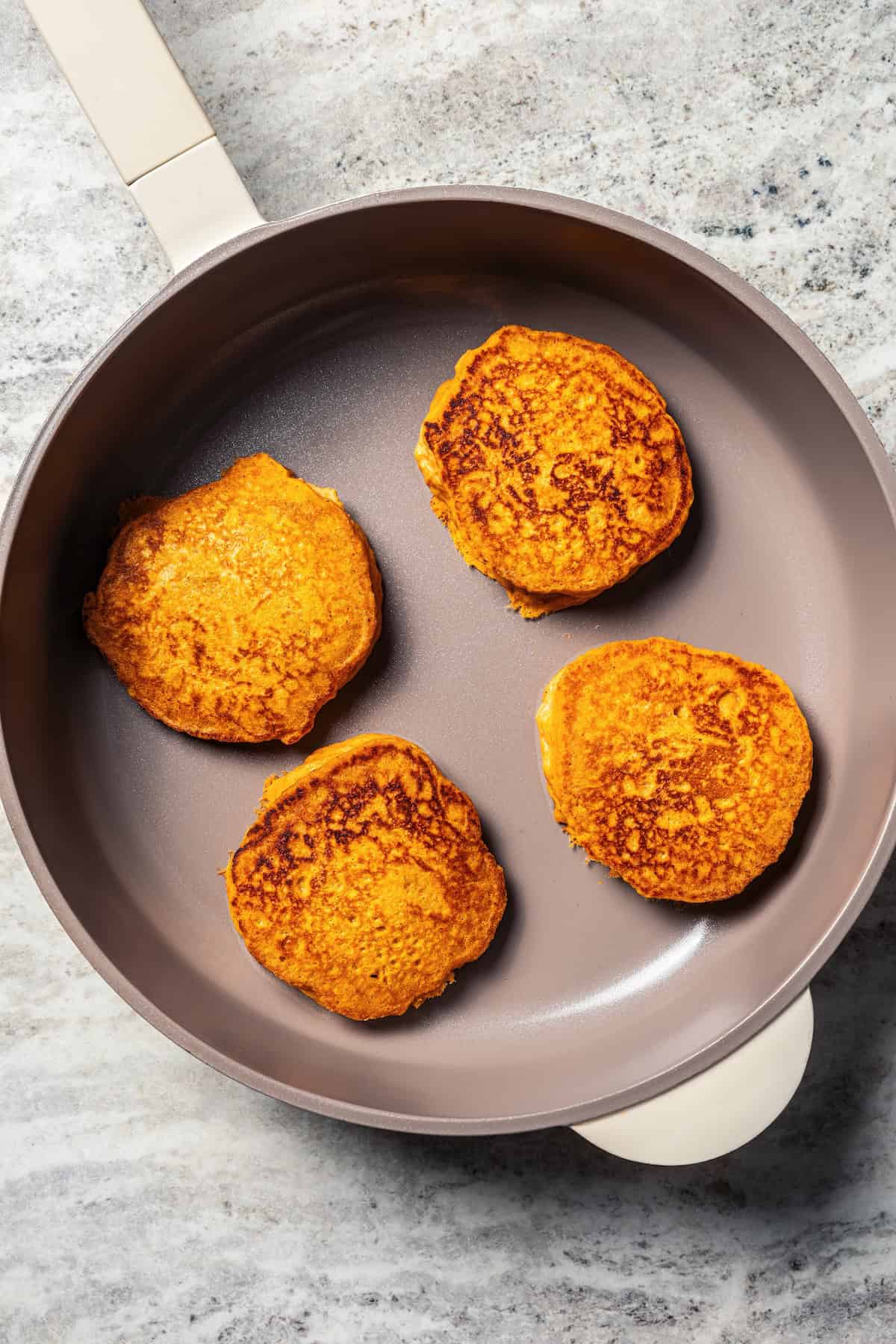 Pumpkin pancakes are the best fall breakfast! Made from pancake mix, real pumpkin, and spices, topped with cranberry syrup for the holidays. Four cooked pumpkin pancakes in a skillet.