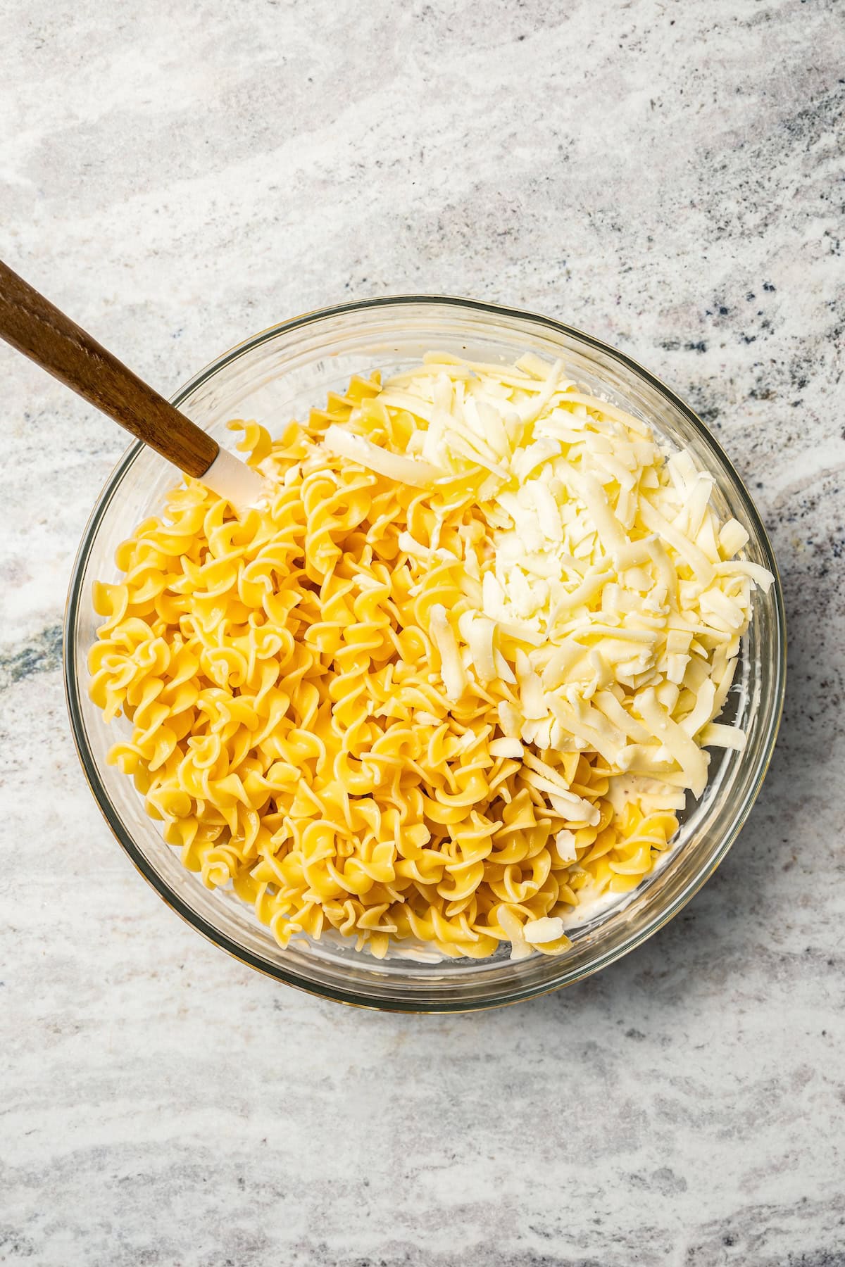 Noodles combined with shredded cheese and the rest of the casserole ingredients in a bowl.