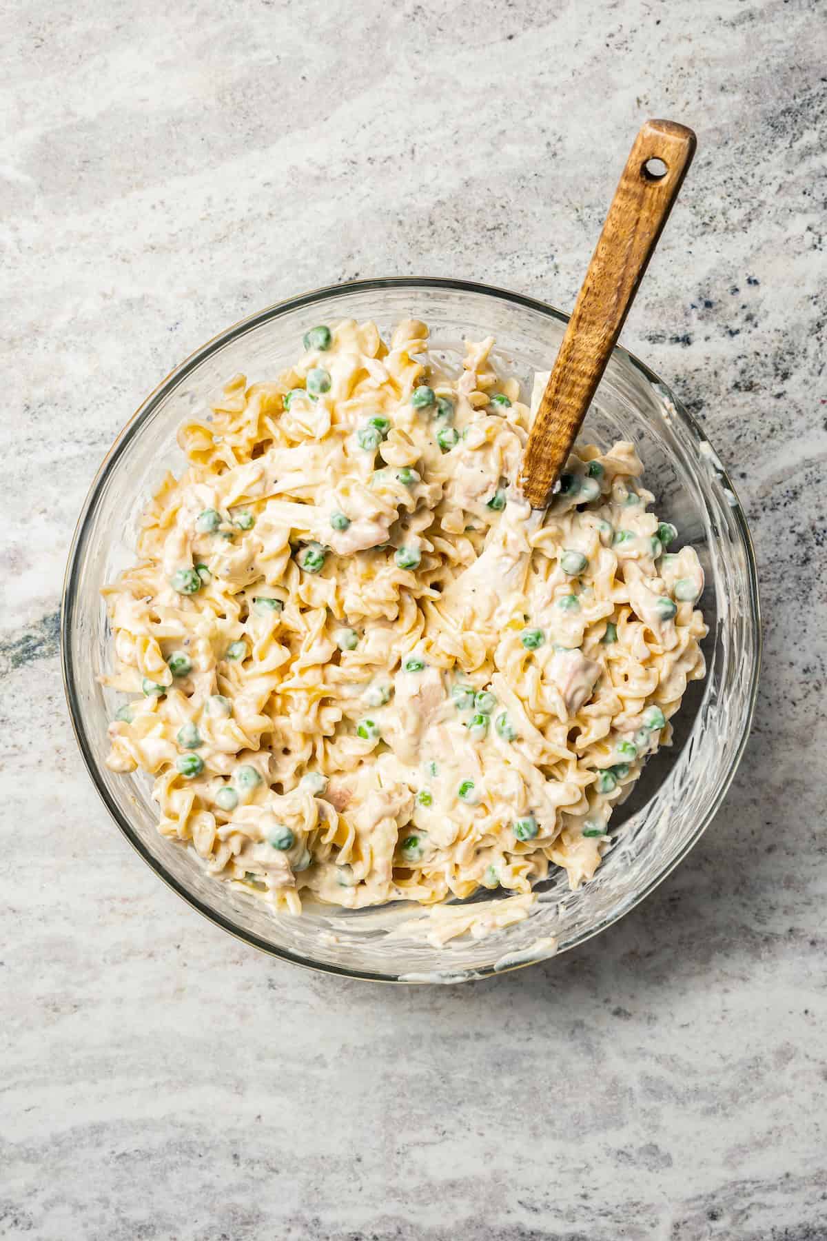 Tuna noodle mixture in a glass mixing bowl with a spoon.