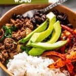 A taco bowl filled with taco fixings, including browned ground beef, rice, avocado, black beans, and peppers.