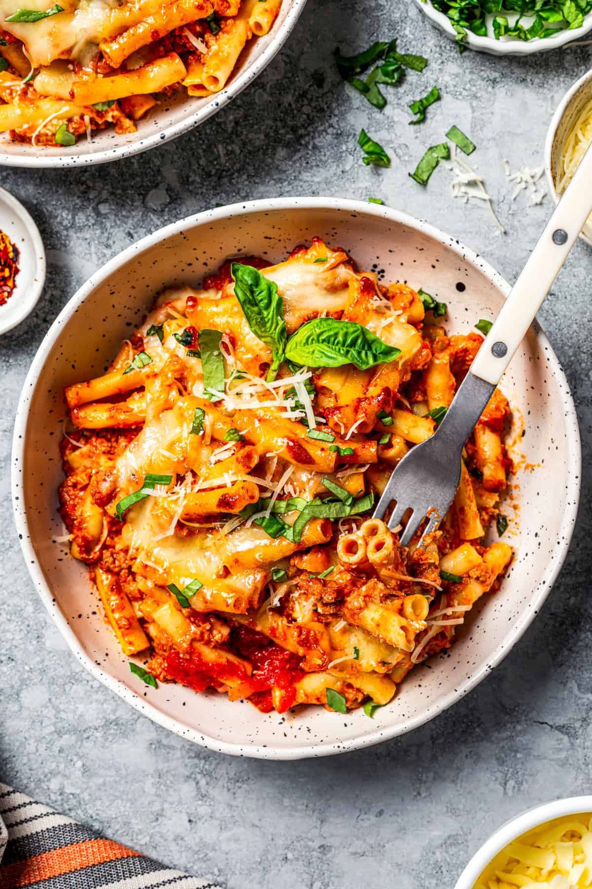 My easy baked ziti recipe is a weeknight-friendly pasta casserole with rich homemade meat sauce and three kinds of melty Italian cheese. Bowl of cheesy baked ziti with a fork resting in the pasta.