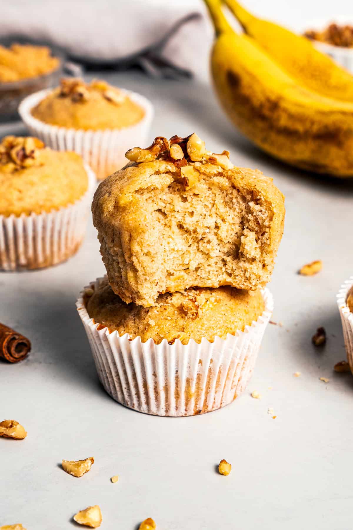 Two banana nut muffins stacked on top of one another, with a bite missing from the top muffin.