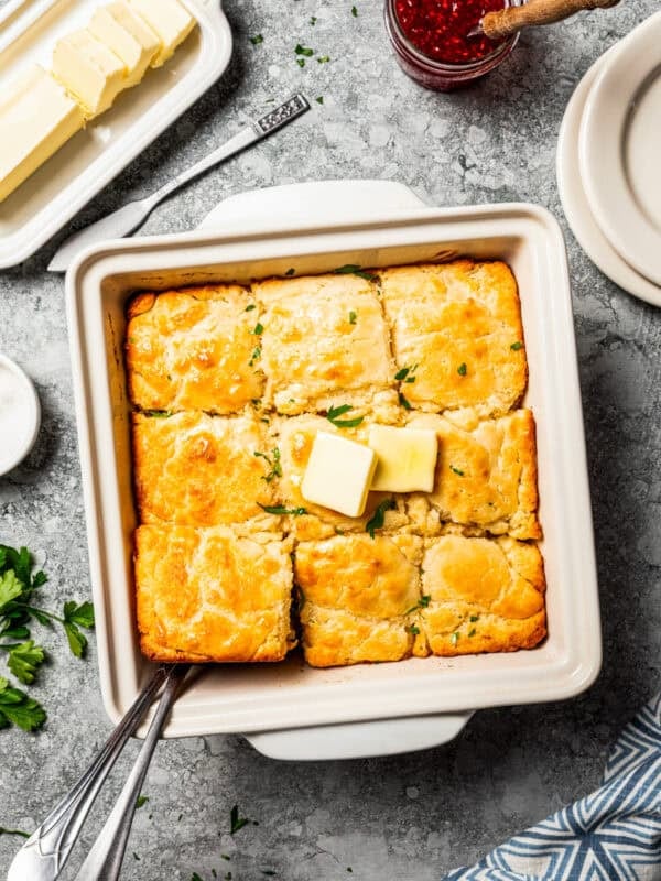Butter swim biscuits topped with pats of butter in a square baking dish.