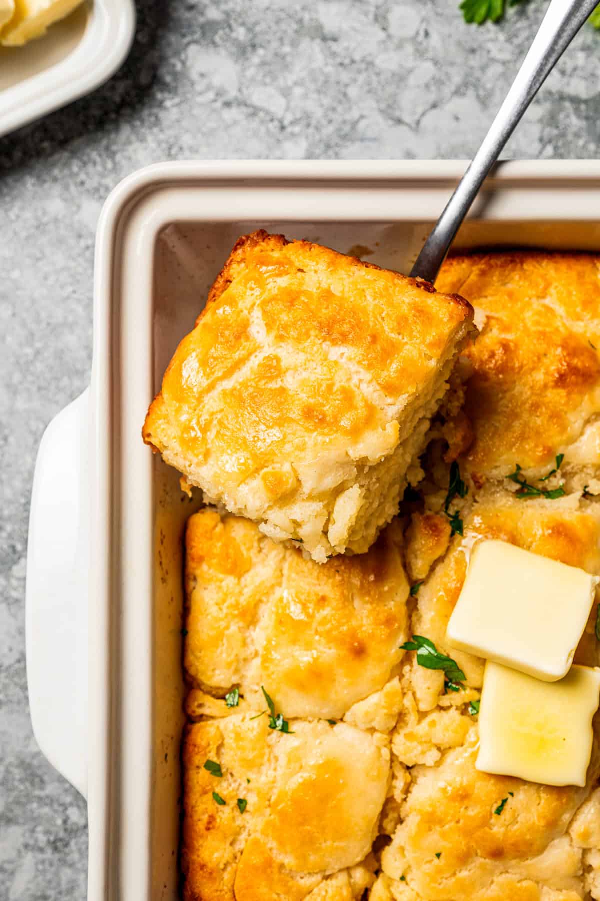 Butter swim biscuits are fluffy drop biscuits baked in a pool of butter! Crispy outside, soft inside, and easy to make with 5 ingredients. Lifting out a butter swim biscuit from the corner of a baking dish.