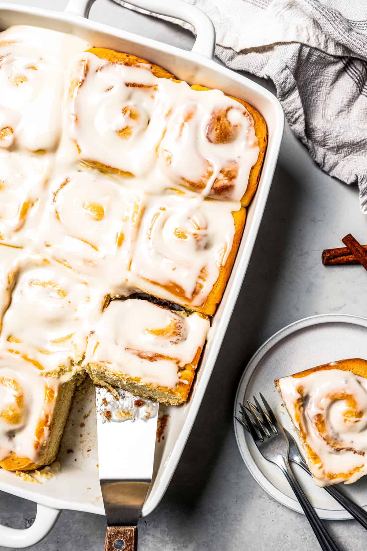 This cinnamon roll recipe makes big, bakery-style cinnamon buns filled with gooey cinnamon sugar and topped with sweet cream cheese frosting. Homemade cinnamon rolls in a baking dish, with one roll missing from the corner, and served on a plate.